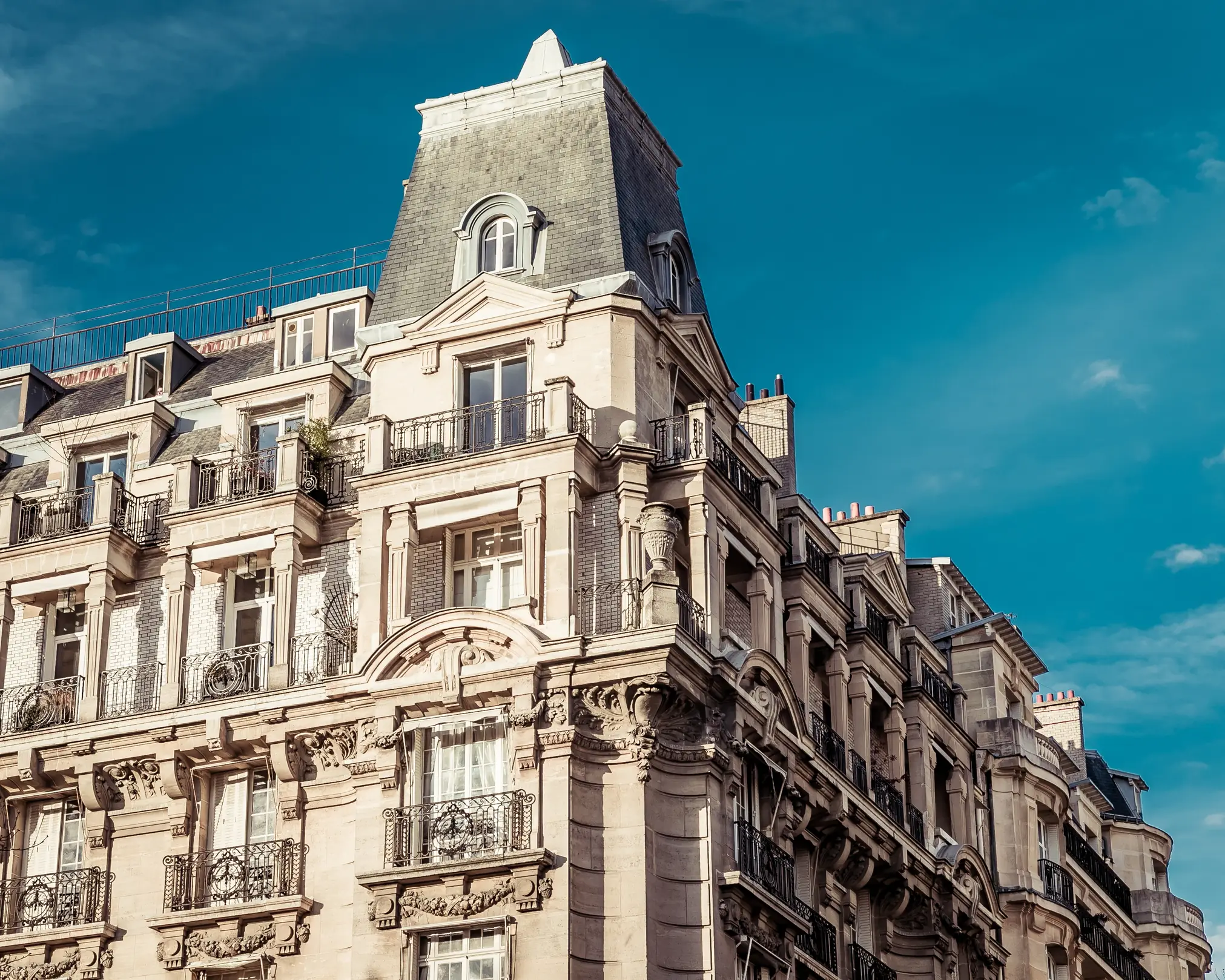 Façade d’un immeuble haussmannien en pierre de taille, sous un ciel bleu.